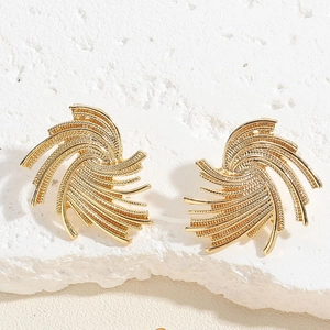 Detailed view of gold fan-shaped stud earrings with textured finish on white stone surface