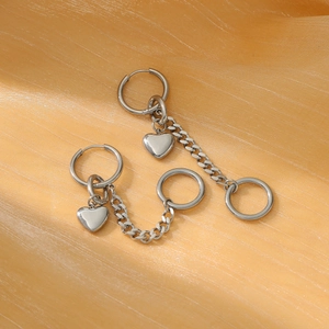 Detail of silver drop earring with heart pendant and metal chain on gold silk fabric