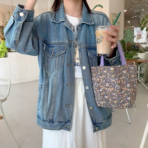 Detail of retro floral corduroy tote bag held by model wearing a denim jacket