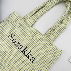 Detail of yellow and blue checkered tote bag with ruffled handles and Sozakka text logo