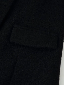 Detail shot of black woolen boucle coat fabric with a structured flap pocket design
