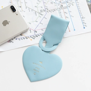 Close-up of a light blue faux leather heart luggage tag on a travel map background