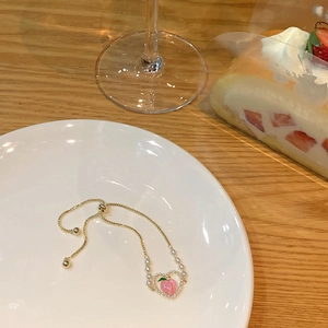 Detalle de pulsera dorada ajustable con dije de corazón de melocotón y perlas en plato