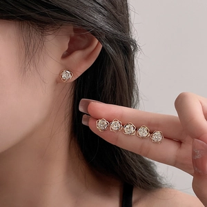 Macro shot of 6-piece gold rose stud earrings set with zircon stones on model's ear