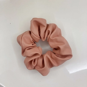 Detail shot of a soft pink PU leather scrunchie with smooth texture and vintage look