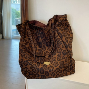 Close-up of leopard print suede tote bag featuring a golden oval brand logo plate