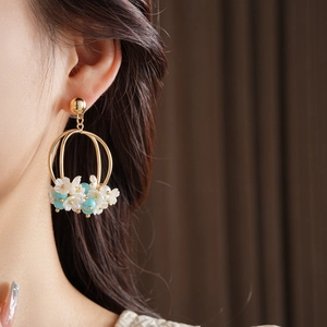 Close-up of golden hoop earrings featuring delicate white flowers and blue beads on model