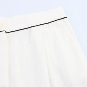 Detailed macro view of white linen pants featuring black contrast piping and button closure