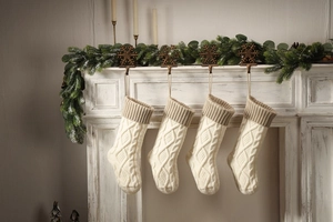 Set of four cable-knit Christmas stockings in cream and brown hanging on a white fireplace