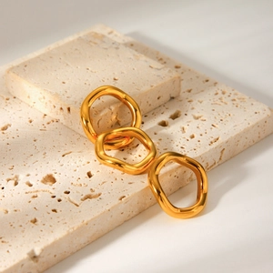 Detailed view of three gold-plated wave rings set on a travertine stone pedestal