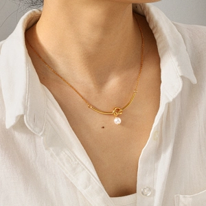 Collana con pendente a nodo e perla in oro 18k indossata da una modella su lino bianco