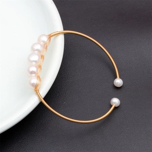 Detail of mixed-color freshwater pearls on a golden spring coil bracelet on a ceramic plate