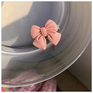 Close-up of a pink matte bow hair clip placed on a metallic disc with soft natural side lighting