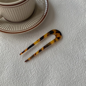 Épingle à cheveux en U motif écaille de tortue à côté d'une tasse sur fond texturé