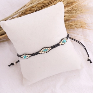 Bohemian woven seed bead bracelet in turquoise and gold on a white display cushion