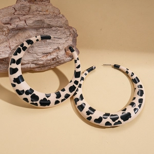 Detailed close-up of large C-shaped hoop earrings with cow print resin texture on rock base
