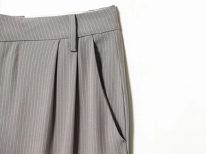 Detail of grey pinstripe trousers featuring pleated waist and side pockets
