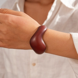 Detailed view of an irregular organic resin bangle in dark brown on a model wrist