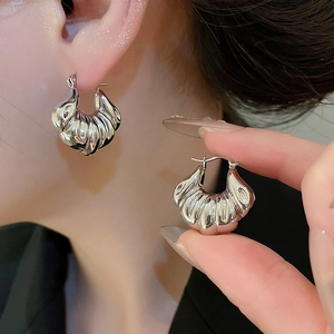 Macro detail of silver shell-shaped croissant hoop earrings with a polished metallic finish