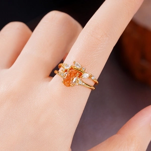 Detailed close-up of a gold ring with orange oval gemstone and diamonds on a finger