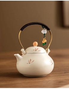 Detail of cream ceramic teapot with floral pattern and braided rope handle with jade pendant
