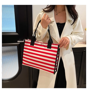 Detail of red and white striped canvas tote bag with black straps and metal snap closure