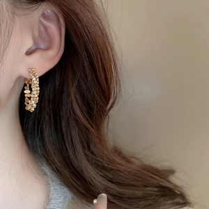 Close-up of a gold-toned C-shaped earring with intricate zircon pavé worn by a model