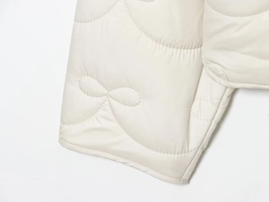 Detail of cream quilted jacket showing intricate gourd patterns and fine stitching texture
