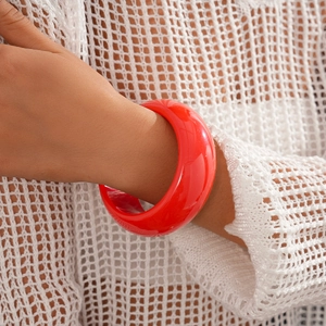 Detail view of bold red resin bangle bracelet on wrist with elegant knit sleeve