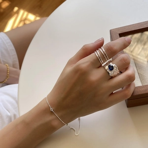 Detailed view of layered 925 sterling silver rings and a slim chain bracelet on hand