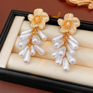 Détail de boucles d'oreilles fleurs dorées avec pompons de perles blanches en boîte