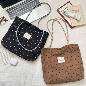 Detail of corduroy tote bags with colorful beaded straps and bow heart patterns