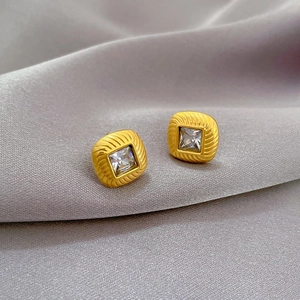 Detail shot of golden square stud earrings with cubic zirconia on grey silk fabric