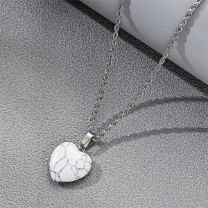 Collier avec pendentif coeur en marbre blanc posé sur un fond texturé gris élégant