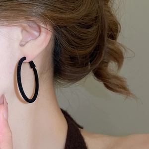 Detailed view of large black flocked hoop earring worn by a model on plain background