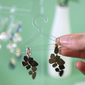 Golden leaf-shaped earrings displayed on a transparent mini clothes hanger stand