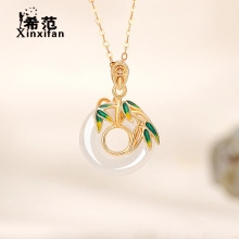 Close-up of gold chain necklace with round white jade pendant and green bamboo leaf motif