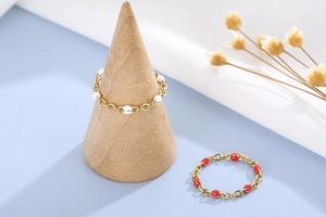 Dettaglio di anelli a catena dorata con eleganti perle in resina bianche e rosse