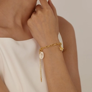 Detail of a gold stainless steel bracelet featuring white shell and starfish charms on wrist