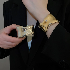 Close-up of irregular liquid metal gold and silver wide bangles on a black suit sleeve