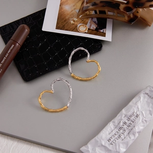 Close-up of asymmetrical heart earrings with two-tone hammered texture and artistic finish