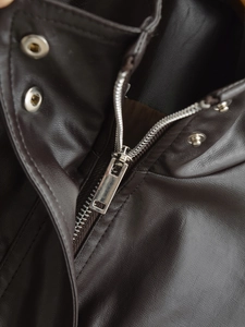 Detailed close-up of a silver metal zipper on a dark brown faux leather jacket with texture