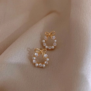 Detailed macro view of bow-knot pearl earrings with micro-set zircons on gold metal