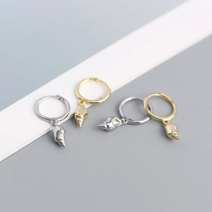 Macro shot of gold and silver conch shell charm hoop earrings on a neutral background