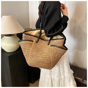 Close-up of a large straw tote bag featuring black shoulder straps and trim details