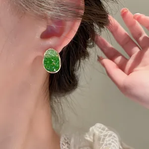 Close-up of irregular green crystal earrings with gold trim on model wearing lace