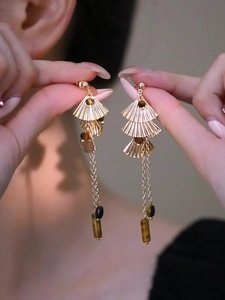 Détail de boucles d'oreilles pendantes à pompon avec pierre œil de tigre et feuille de ginkgo