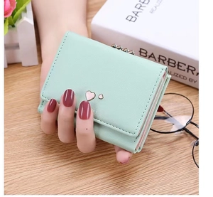 Close-up of mint green tri-fold faux leather wallet with pink heart charm being held