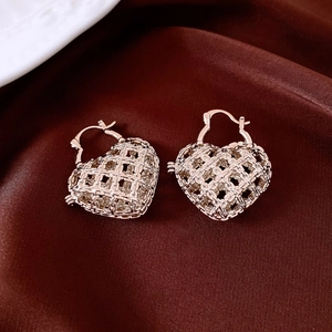 Detailed shot of gold woven mesh heart earrings resting on elegant deep red silk fabric