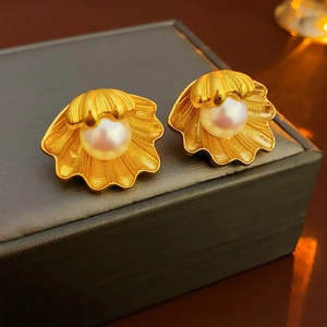 Close-up of golden shell-shaped pearl earrings on a premium jewelry box lid